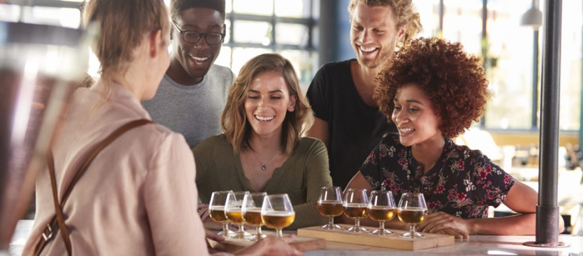 Waitress Serving Group Of Friends Beer Tasting In Bar